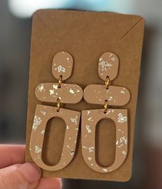 a person holding up a pair of earrings in front of a brown card with the number 50 printed on it