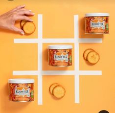 three cans of tea and four cookies on an orange surface with white squares in the middle