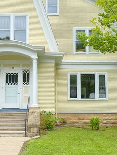 a yellow house with a white door and steps leading up to the front porch area