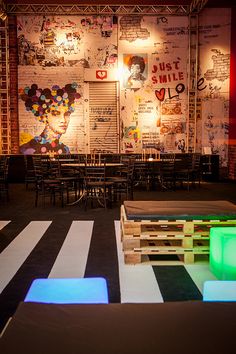 an empty room with tables and chairs lit up by colorful lights on the wall behind them