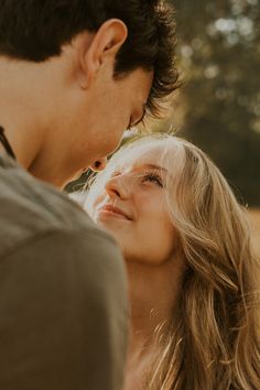 a man standing next to a woman with long blonde hair looking at her face and smiling