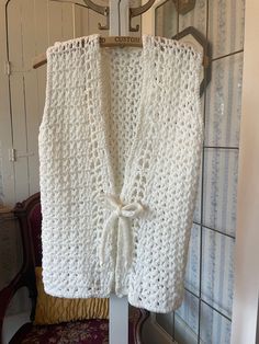 This vest was crocheted by hand from an acrylic yarn in pure white, in a fairly open stitch. It has a matching tie at the waist. The measurements, taken with the vest lying flat, are: shoulder to shoulder, 13 1/2 inches; armpit to armpit, 17 inches; length, 22 inches; bottom edge, 19 inches. In very good condition. White Bohemian Crochet Vest Top, White Knitted Vest For Summer, White Knitted Vest For Spring, Summer Knitted White Vest, Handmade White Sleeveless Crochet Top, White Knitted Summer Vest, White Handmade Sleeveless Crochet Top, White Crochet Vest For Spring, White Crochet Vest For Summer