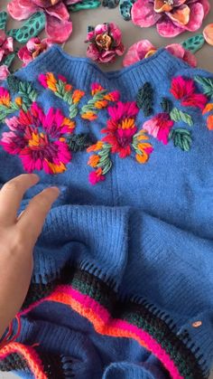 someone is holding their hand over the top of a blue sweater with flowers on it