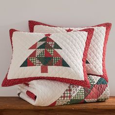 three pillows with christmas trees on them sitting on a wooden shelf next to a white wall