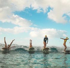 four people on surfboards in the water with their hands up and one person standing on top of them