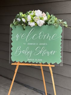 a welcome sign for a baby shower with flowers on it and greenery in the center