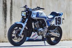 a white and blue motorcycle parked on the side of a road next to a wall