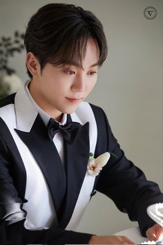 a young man in a tuxedo cutting a cake with a flower on it