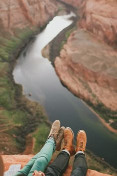 two people sitting on the edge of a cliff with their feet up in the air