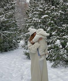 a woman holding a stuffed animal in her arms while standing next to snow covered trees