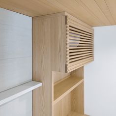 a wooden shelf sitting next to a window in a white walled room with wood slats on the wall