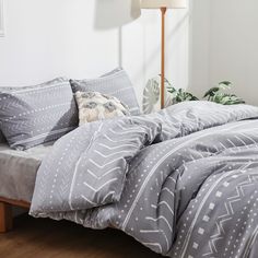 a bed with grey and white comforters in a room next to a lamp on a wooden floor