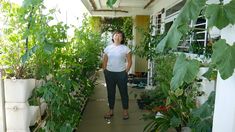 a woman standing in the middle of a room filled with plants and potted plants