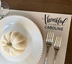 a white plate topped with a pumpkin next to silverware and a thank you card