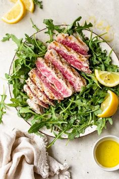 a white plate topped with meat and greens next to lemons on a counter top