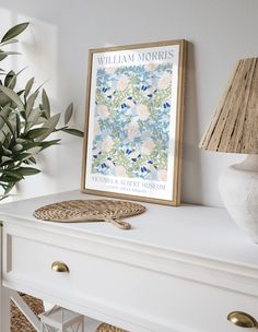 a white dresser topped with a vase filled with flowers and a framed poster on top of it