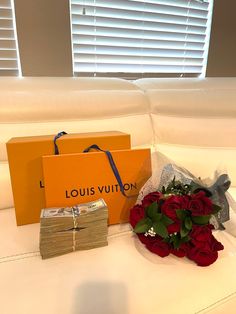 a bouquet of red roses sitting on top of a white couch next to two orange boxes