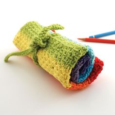 crocheted rolled up cloths with colored pencils next to them on a white surface