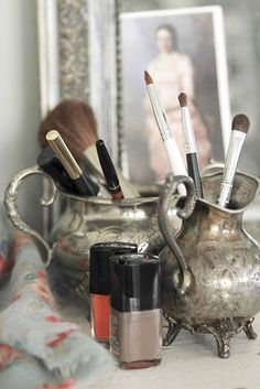 a silver vase filled with makeup brushes and other items next to an image of a woman's face