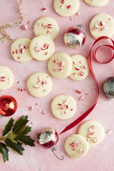 white buttons with red and white sprinkles next to christmas decorations on a pink surface