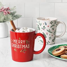 two christmas mugs with marshmallows and cookies on the side next to them