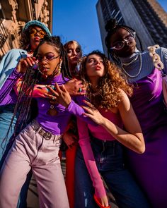 a group of young women standing next to each other in front of tall buildings with their arms around one another