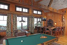 a pool table in the middle of a room with wooden walls and ceilings, along with leather chairs