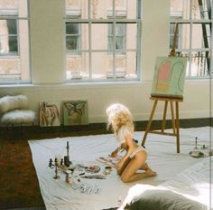 a woman sitting on top of a bed next to an easel