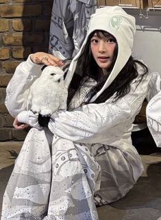 a woman in white is holding an owl