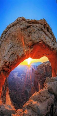 the sun is shining through an arch in the mountain side with rocks and rock formations