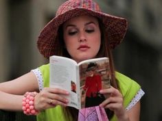 a woman reading a book while wearing a hat