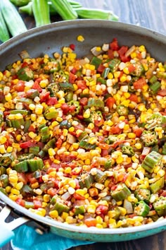 a skillet filled with corn and vegetables on top of a wooden table next to green beans