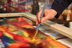 a person is painting on a canvas with a brush and watercolors in the background