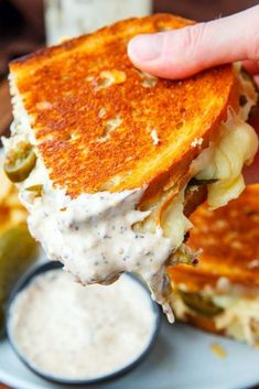 a person is holding up a grilled cheese sandwich with pickles and ranch dressing