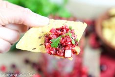 a person holding up a tortilla with fruit salsa on it and garnished with cilantro