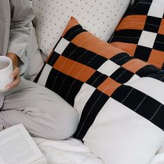 a person sitting on a bed holding a coffee cup and reading a book with an open book beside them