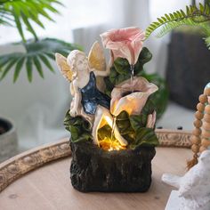 a small fountain with flowers and angel figurines on it sitting on a table