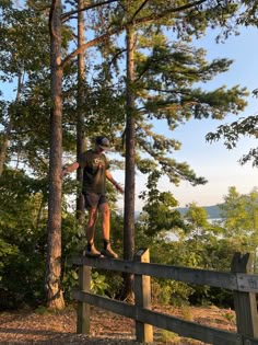 a man standing on top of a wooden fence in the woods next to some trees