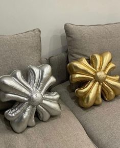 two silver and gold pillows sitting on top of a gray couch next to each other