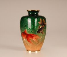 a green and gold vase with red fish on it's side, sitting on a white surface