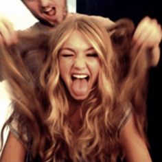 a woman with her hair blowing in the wind as a man looks on behind her