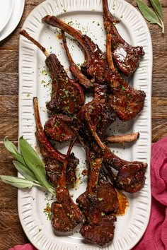 a white plate topped with ribs covered in sauce and garnished with green leaves