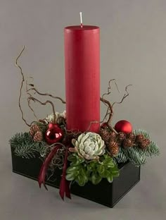 a red candle sitting on top of a black container filled with greenery and ornaments