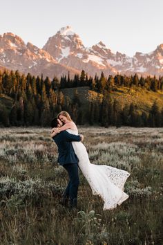 a man and woman hugging in the middle of a field with mountains in the background