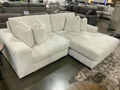 a white sectional couch with pillows on display at a furniture store in the middle of a room filled with sofas