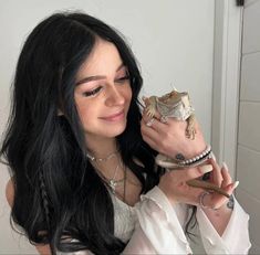 a woman with long black hair holding a lizard in her hand and smiling at the camera