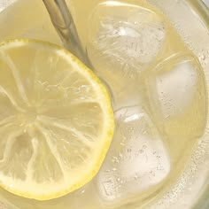 a lemon slice is sitting on top of ice in a glass with water and silver spoon