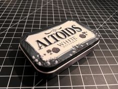 an altoids tin sitting on top of a black and white tiled floor next to a knife