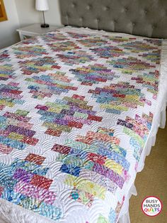 a bed with a quilt on top of it and a lamp in the corner next to it