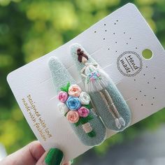 a person holding up two pins with flowers on them and one has a small doll in the middle